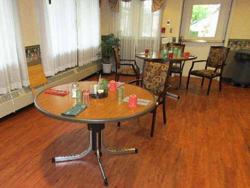 A cozy community dining area featuring several tables and chairs, with natural light streaming in through the windows.