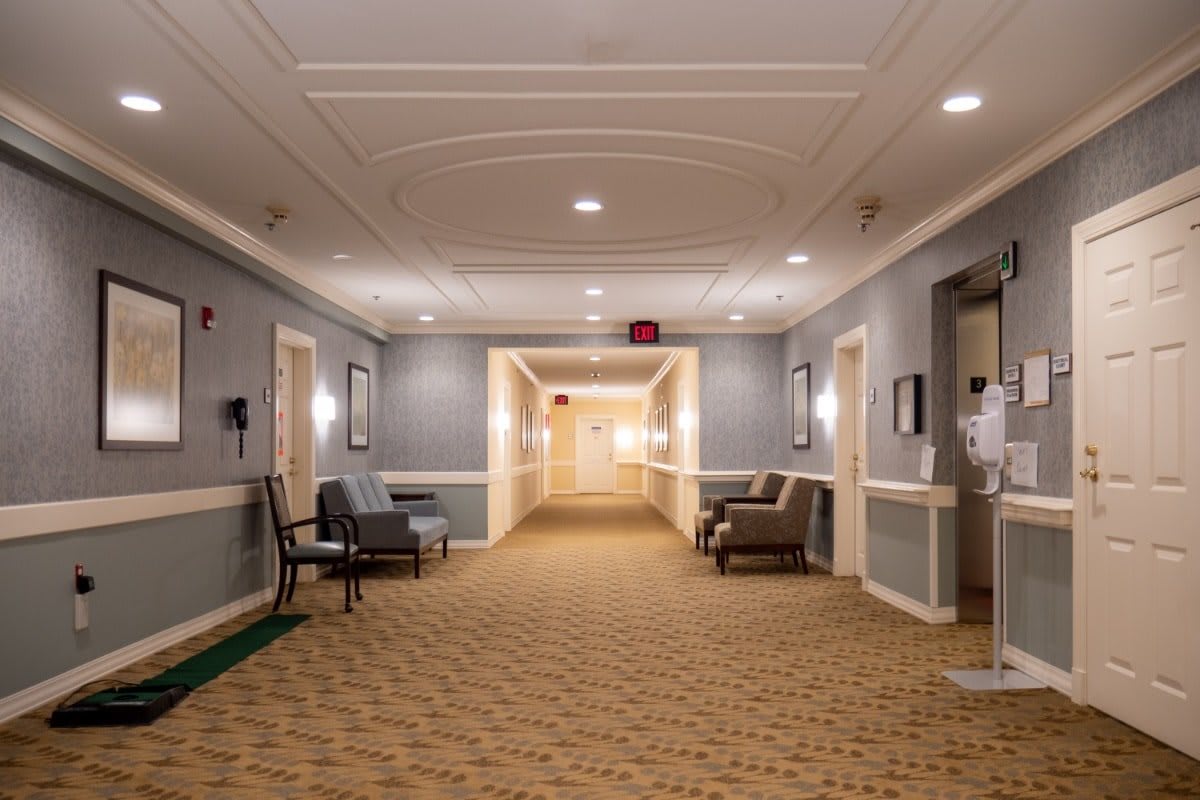 A well-lit hotel hallway with chairs and a patterned carpet.