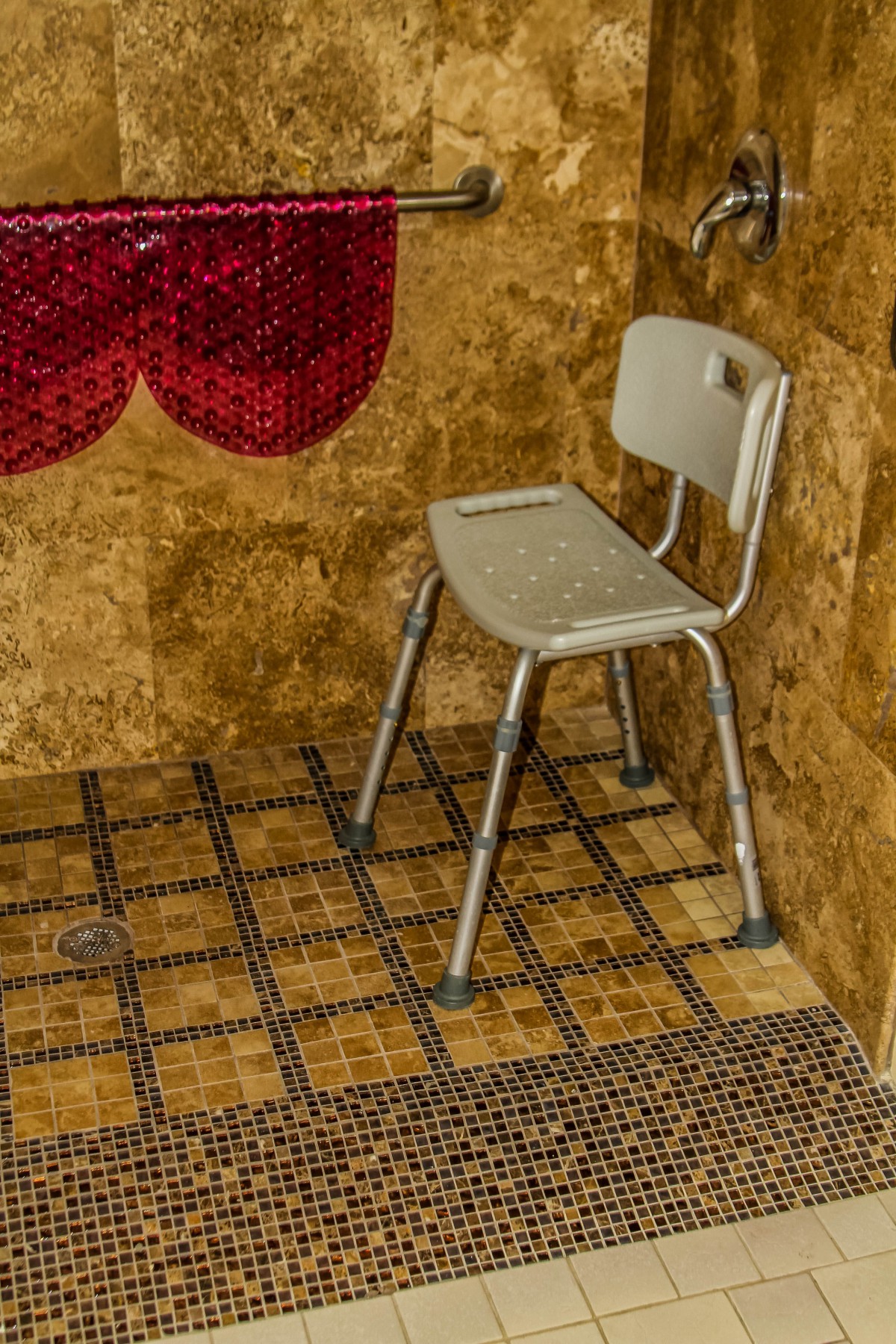 A white chair is placed in a bathroom with mosaic tiled walls and floor.