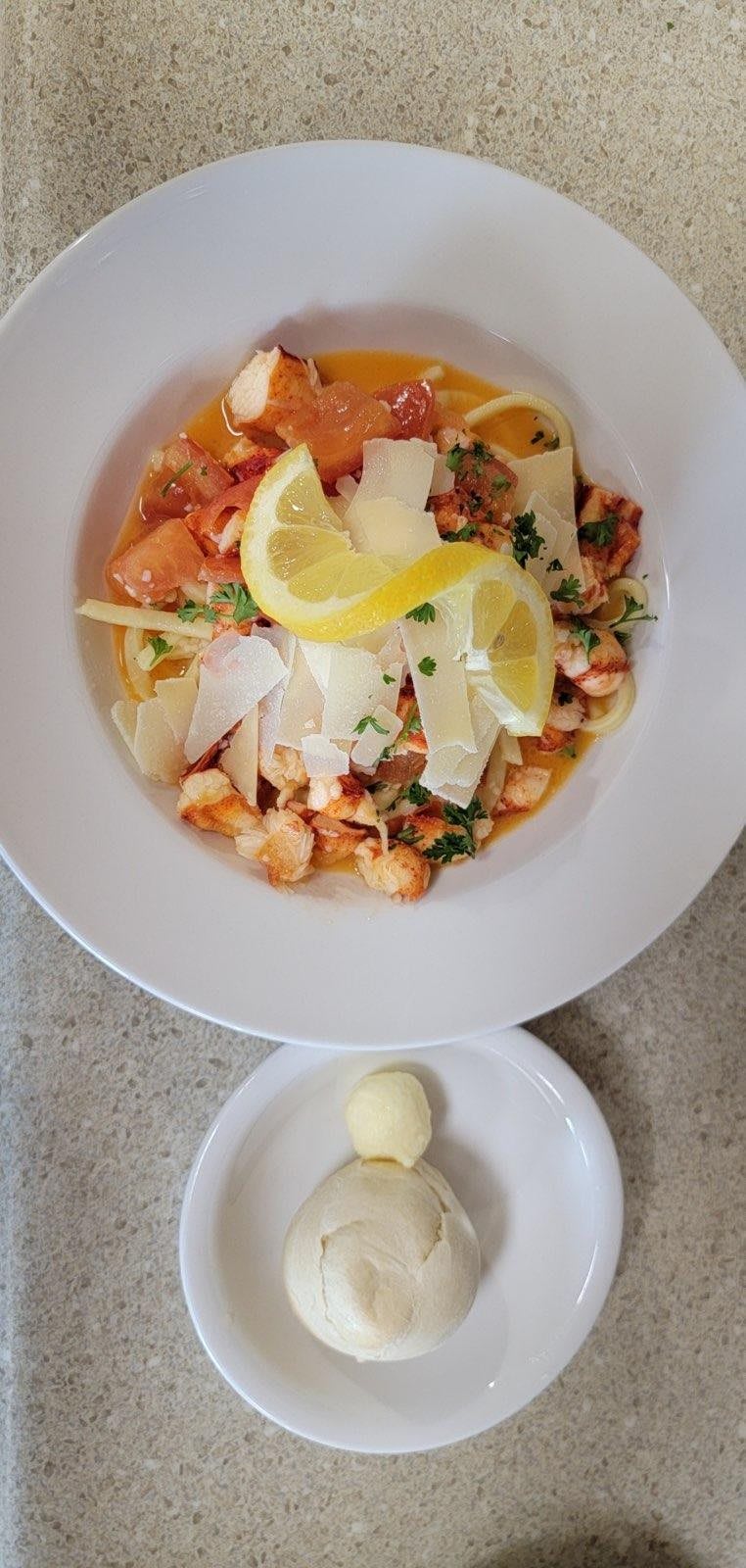 A plate of seafood pasta topped with salmon, lemon slices, and cheese shavings.