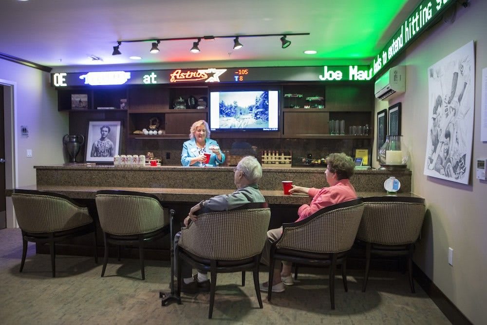 Three people enjoying a conversation at a bar with neon lights and a TV screen in the background.