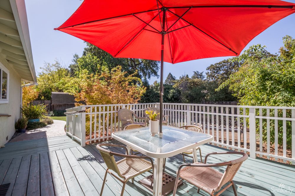 A sunny patio with a table, chairs, and a bright red umbrella.