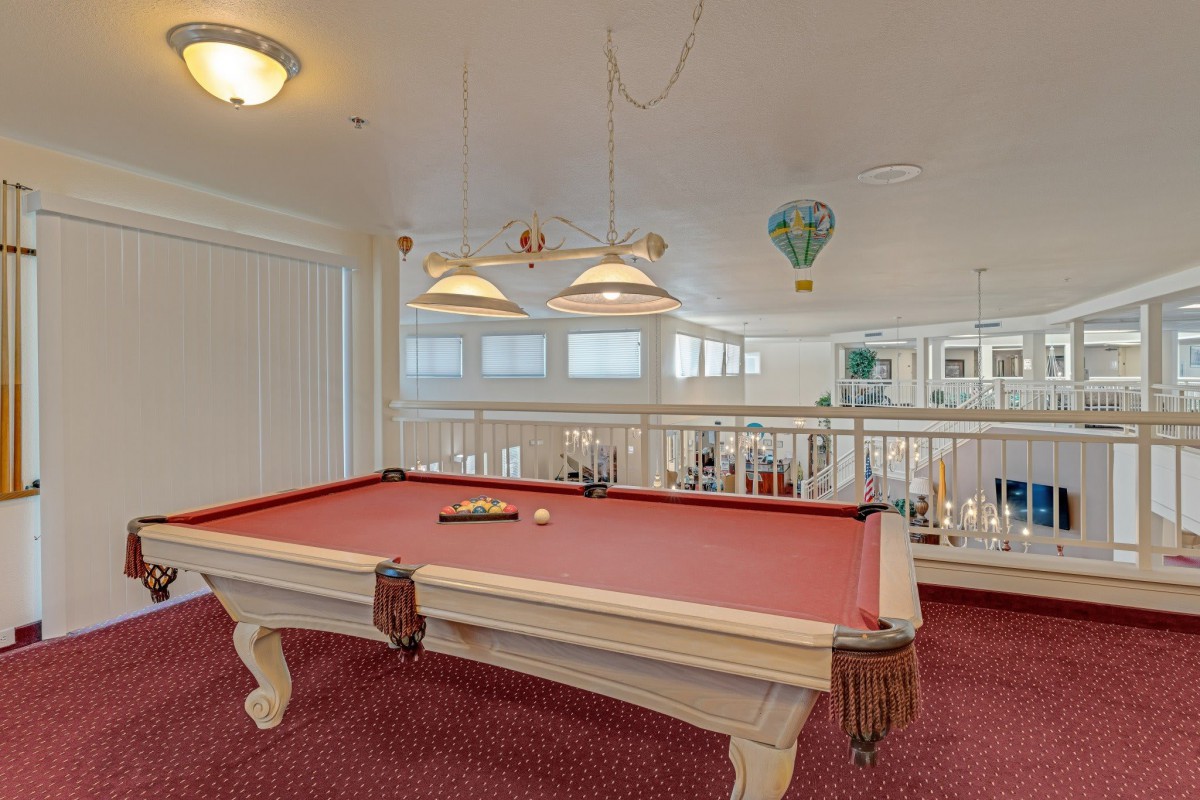 A game room featuring a red pool table with overhead lighting and red carpeting.