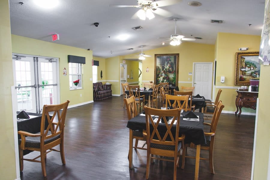 A cozy dining area with wooden tables and chairs, featuring yellow walls and ceiling fans.