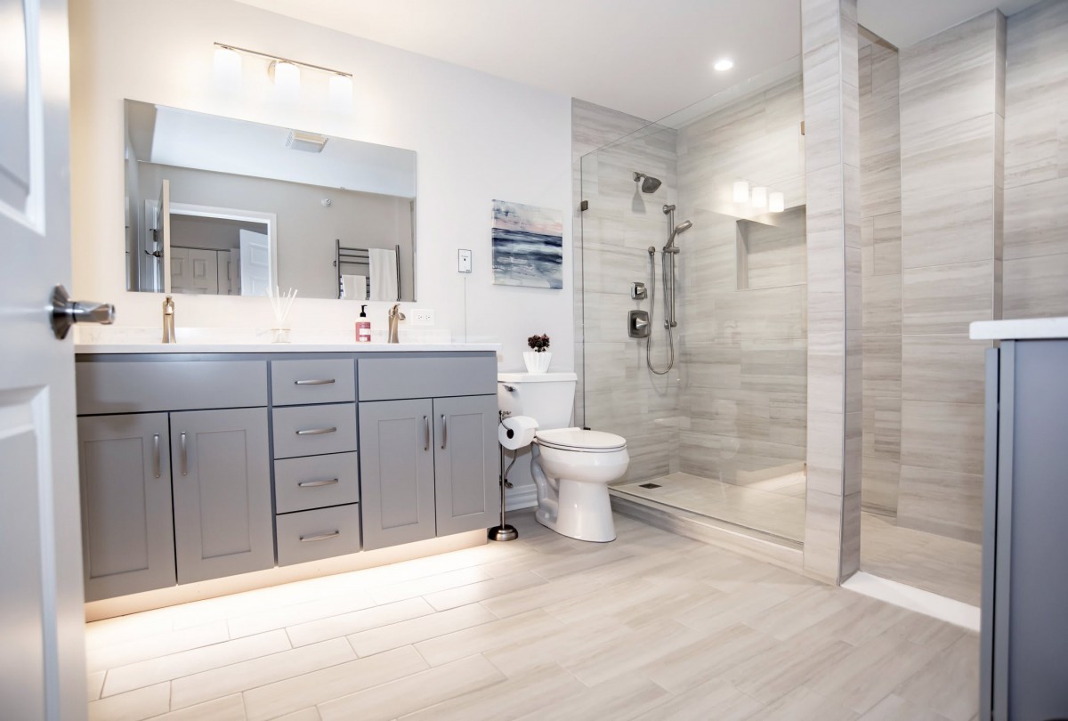 A modern, spacious bathroom with a gray vanity, glass shower enclosure, and minimalist design.