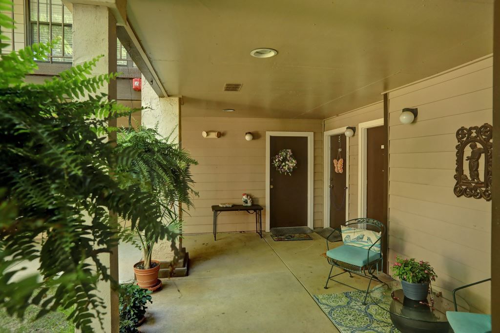 A cozy covered porch with seating, potted plants, and decorated doors.