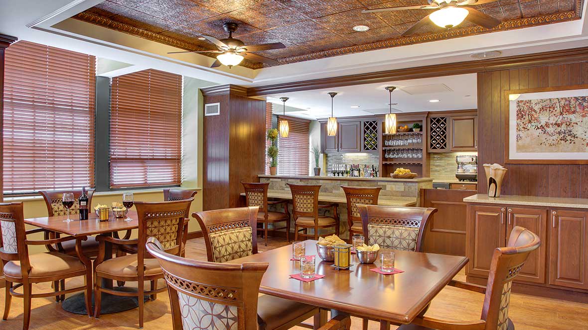 A cozy restaurant interior featuring a dining area with wooden tables and chairs, adjacent to a well-stocked bar.