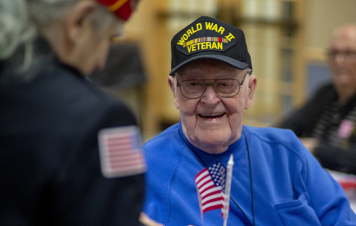 An elderly World War II veteran wearing a hat and holding a small American flag.