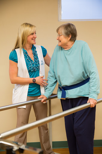 A healthcare professional provides support and assistance to an elderly woman during a rehabilitation session.