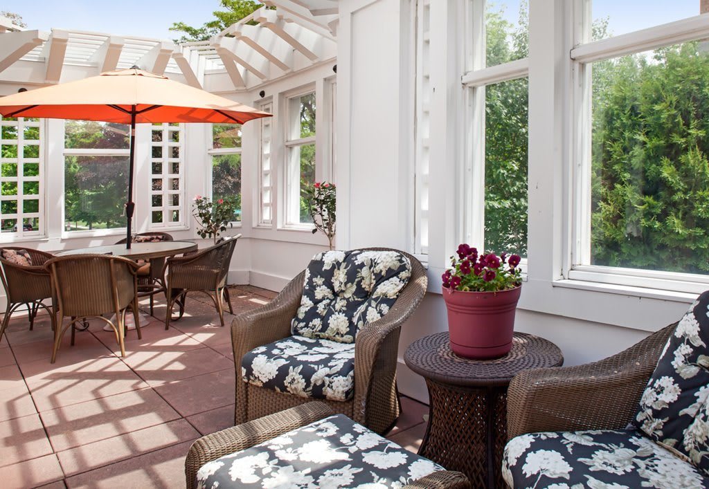 A sunlit patio featuring comfortable seating with floral cushions, a table set, and an umbrella for shade.