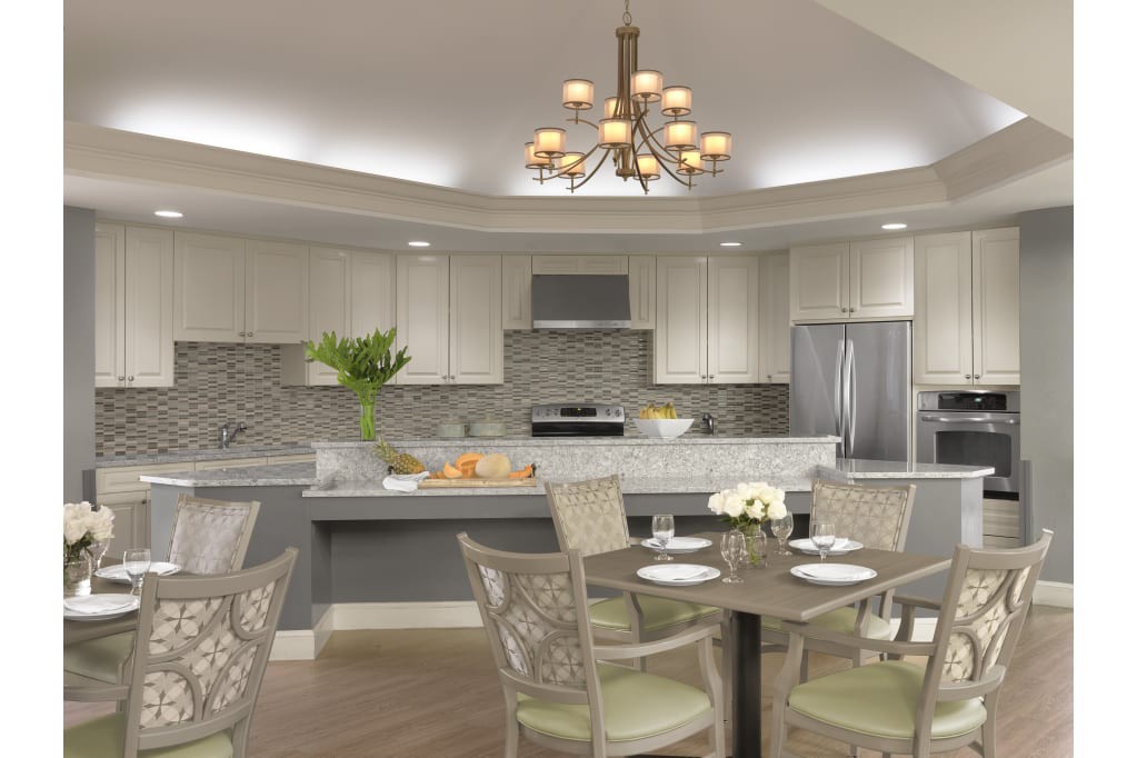 A modern kitchen with a dining area featuring a chandelier, marble countertops, and stainless steel appliances.