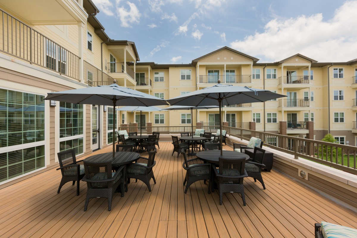 A spacious outdoor patio with tables, chairs, and umbrellas in front of an apartment building.