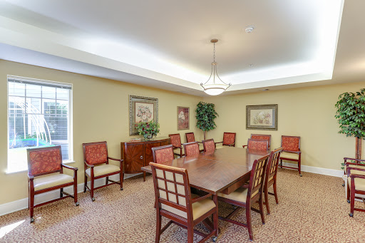 A spacious meeting room featuring a large wooden table surrounded by comfortable red chairs, adorned with artwork and complemented by indoor plants.