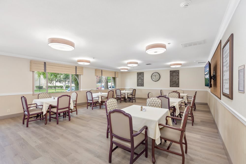 A spacious dining room with neatly arranged tables and chairs, featuring bright lighting and large windows.