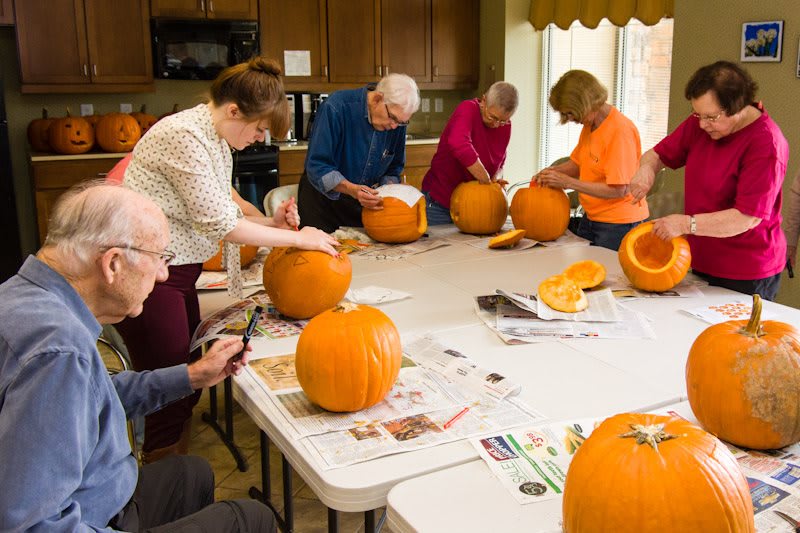 A group of people gathered around a table, engaged in pumpkin carving.