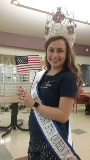 A smiling young woman in a pageant dress holds an American flag, proudly representing her title.