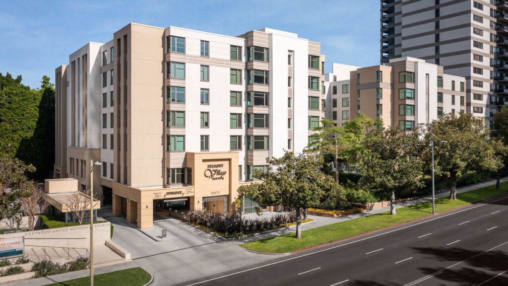 A modern hotel building in an urban setting with surrounding trees and a clear blue sky.