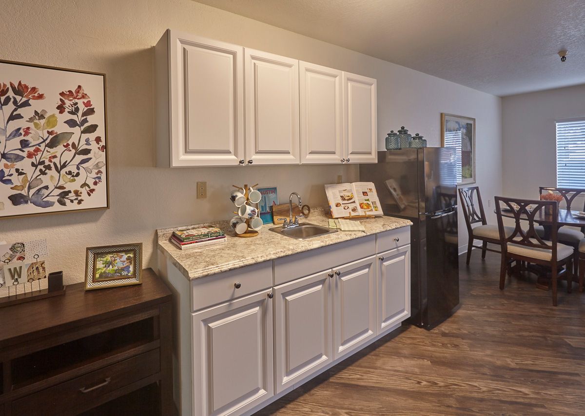 A cozy kitchen space with white cabinets, a colorful countertop display, and wooden flooring.