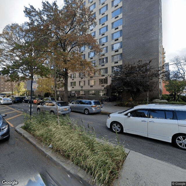 A busy urban street lined with cars, trees, and a tall residential building on an autumn day.