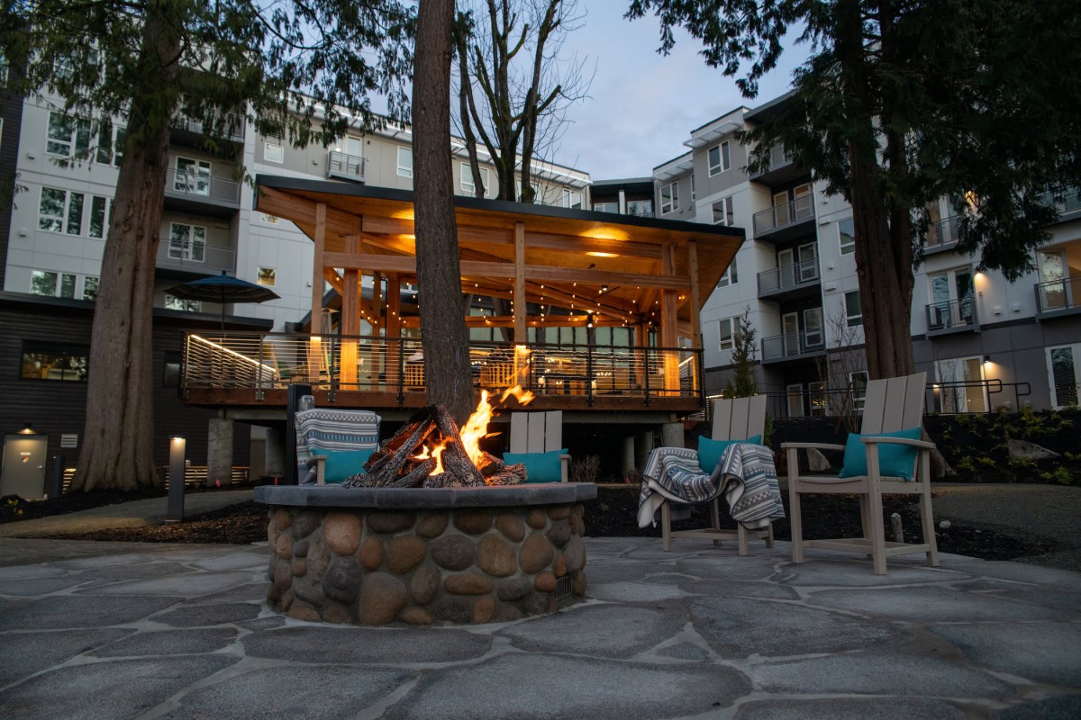A cozy outdoor seating area with a fire pit in front of a well-lit building in the evening.