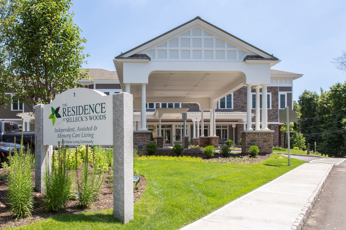 The image shows the entrance of a residential building with well-maintained landscaping and clear signage.