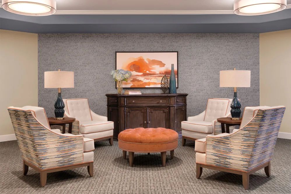 A cozy lounge area with plush chairs, an orange ottoman, and decorative lamps.