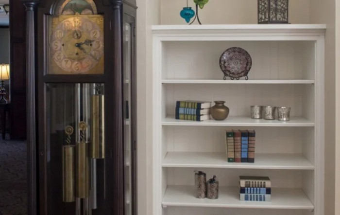 A cozy living space featuring a tall clock and a white bookshelf adorned with books and decorative items.