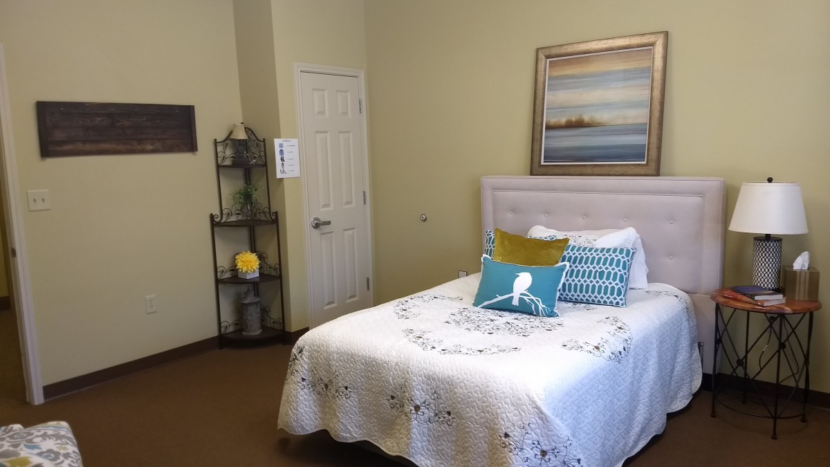 A cozy bedroom featuring a neatly made bed with colorful pillows, a wall painting, and shelves for decoration.