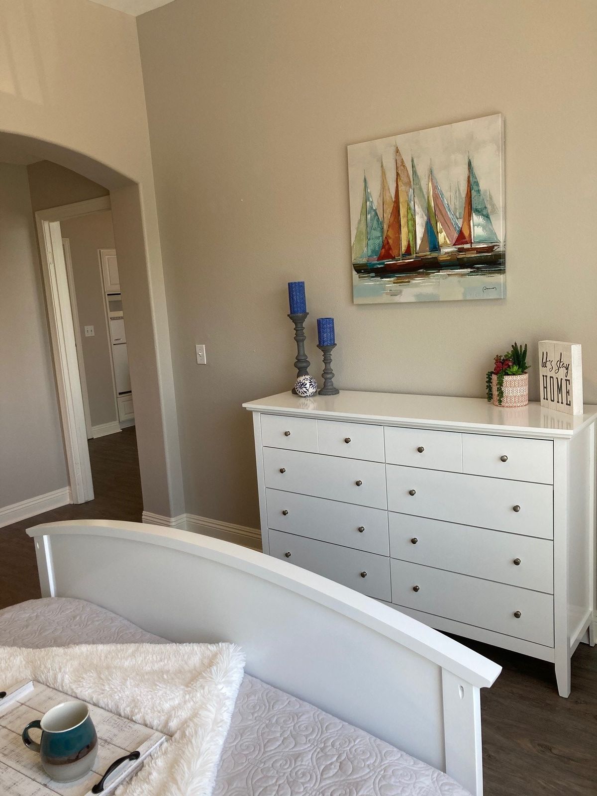 A tidy bedroom with a white dresser, bed, and colorful sailboat painting.