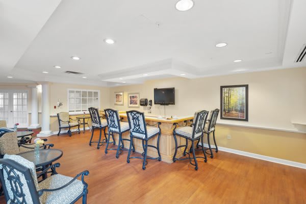 A cozy bar area featuring high chairs, a large counter, and a television, set against warm wooden flooring.