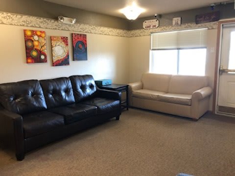A cozy living room featuring a black and a beige sofa, decorated with colorful artwork on the walls.