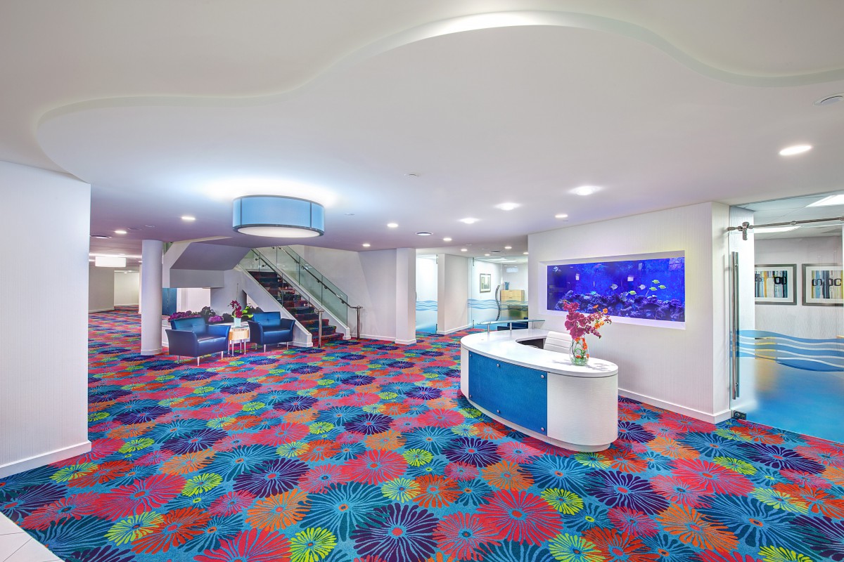 A vibrant hotel lobby featuring a colorful carpet, a modern reception desk, and a large aquarium.