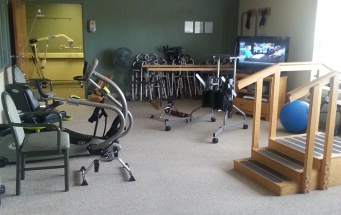 A rehabilitation room equipped with various physical therapy tools including a stationary bike, walkers, and parallel bars.