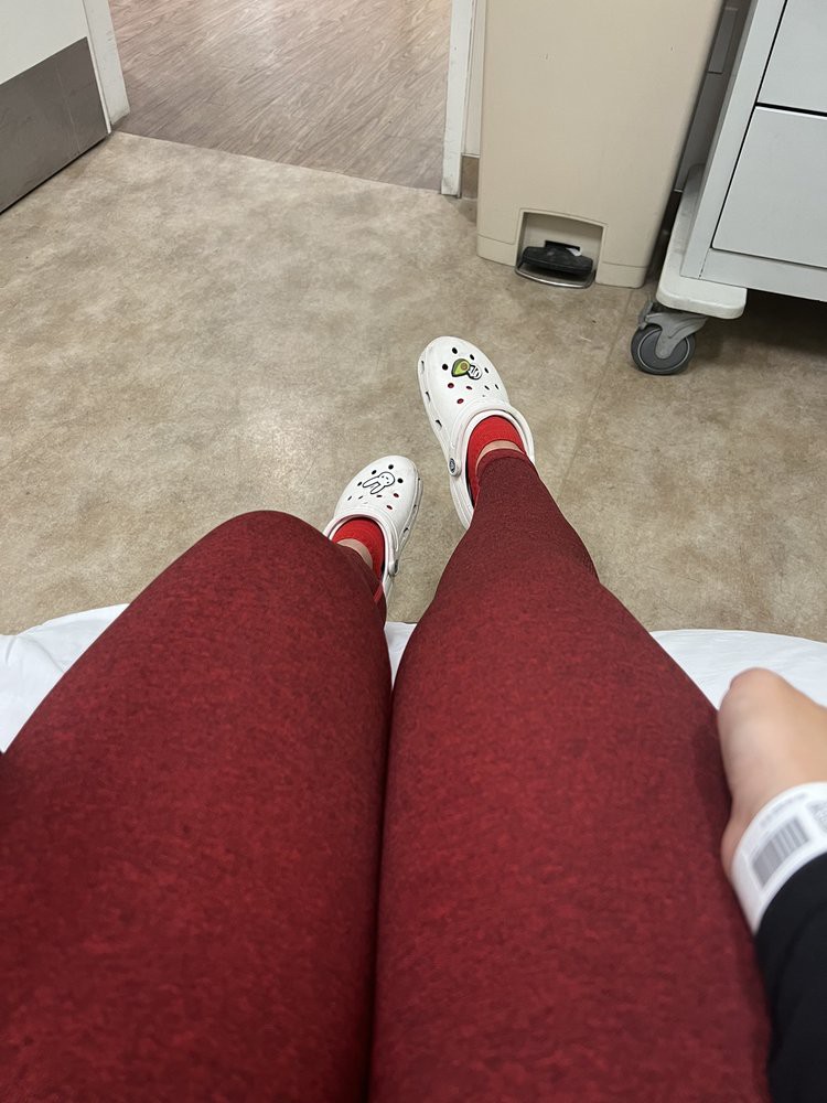 Person sitting on a hospital bed with red leggings and white shoes.