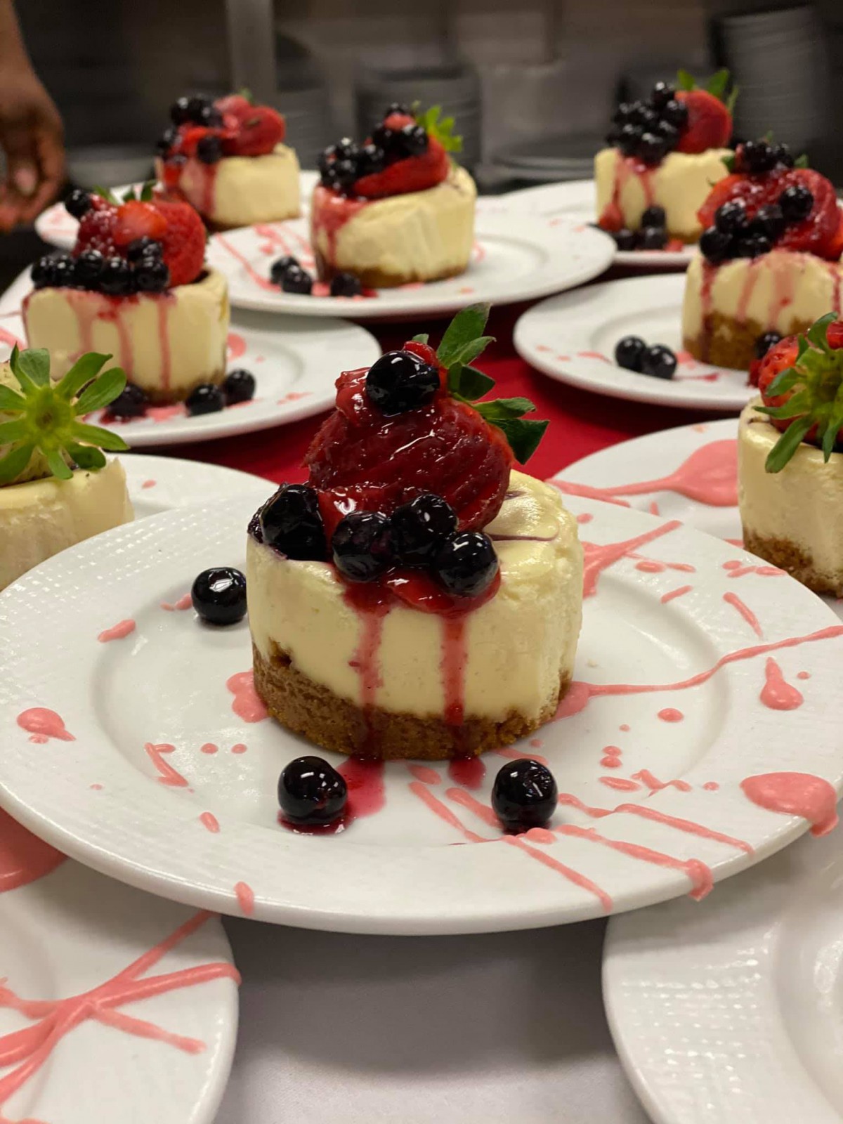 A beautifully plated cheesecake topped with strawberries and blueberries, drizzled with berry sauce.
