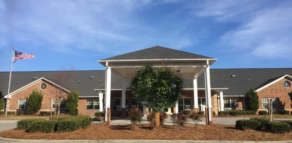 A well-maintained building entrance with a landscaped garden and clear blue sky.