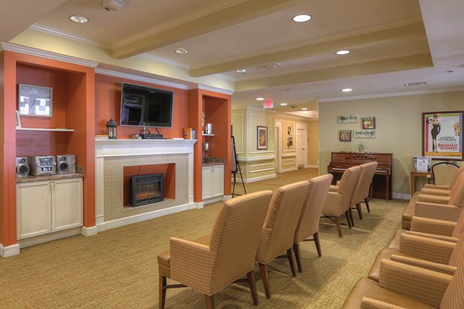 A cozy waiting room with a row of chairs facing a television and fireplace.