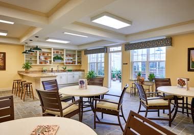A well-lit dining area with tables and chairs, decorative plants, and large windows.