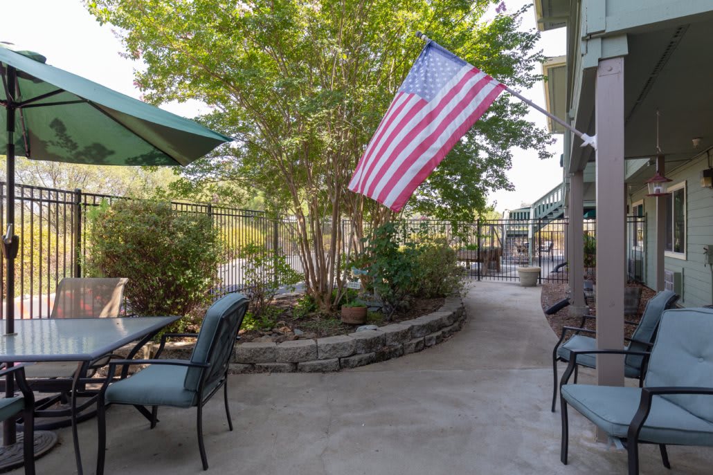 A sunny patio with tables, chairs, and an American flag.