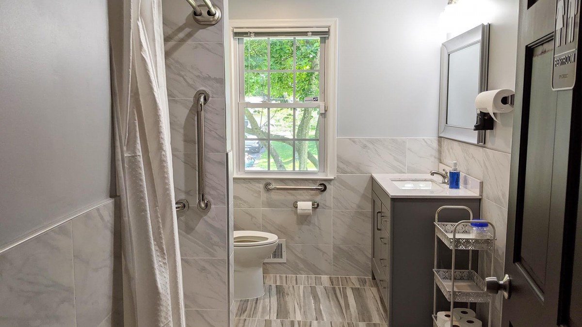 A modern bathroom with a shower, toilet, and sink, featuring marble tiles and a large window.