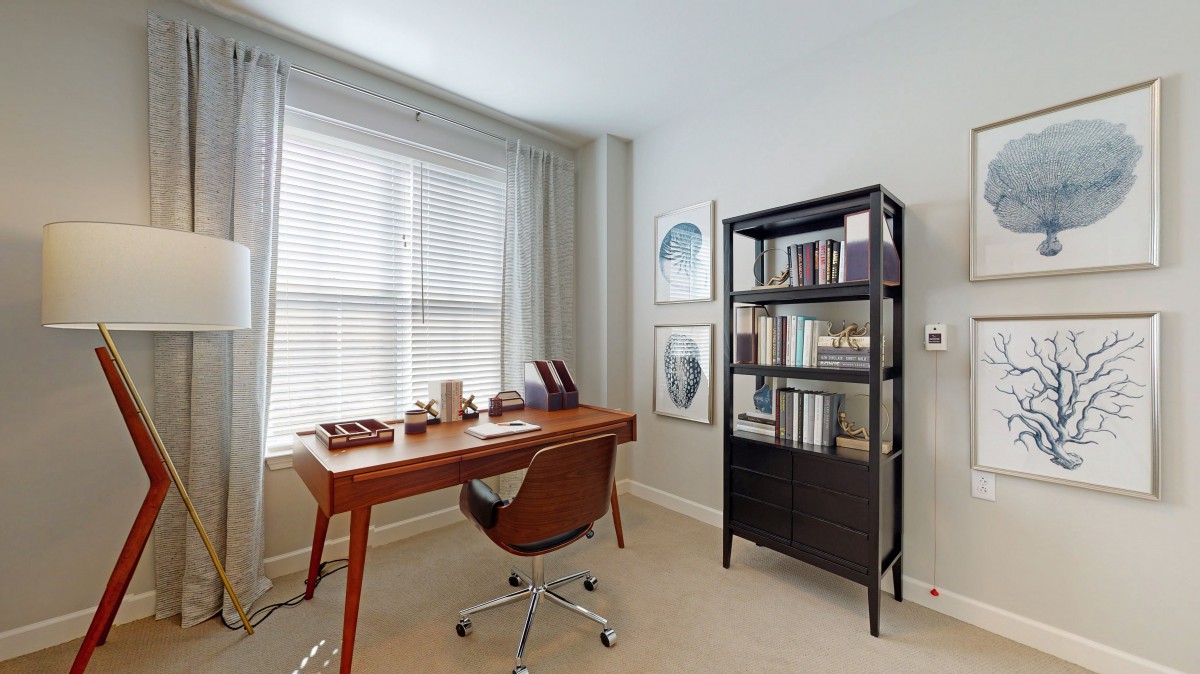 A modern home office with a wooden desk and chair, next to a bookshelf.