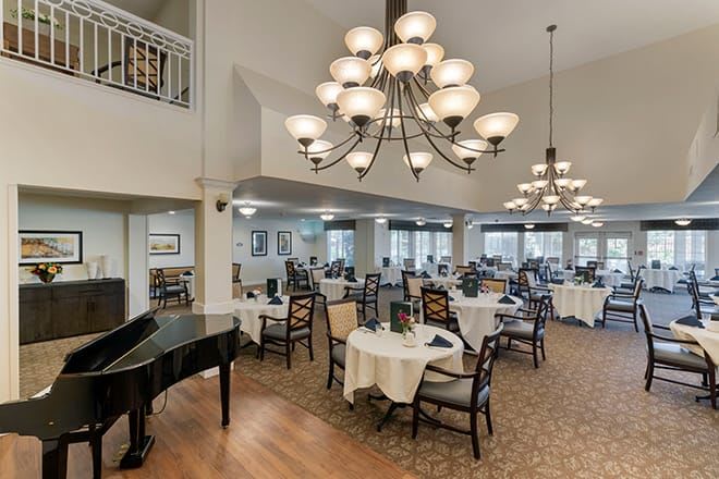 An elegant dining area featuring chandeliers and a grand piano, with tables set for dining.