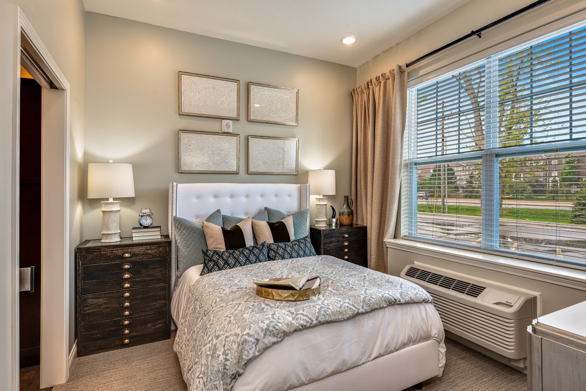 A cozy and elegantly decorated bedroom with a neatly made bed, flanked by two bedside tables and lamps. Large window allows natural light to fill the room.
