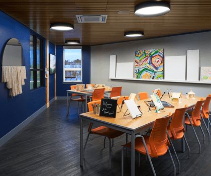 A modern classroom with orange chairs, interactive boards, and colorful artwork on the walls.