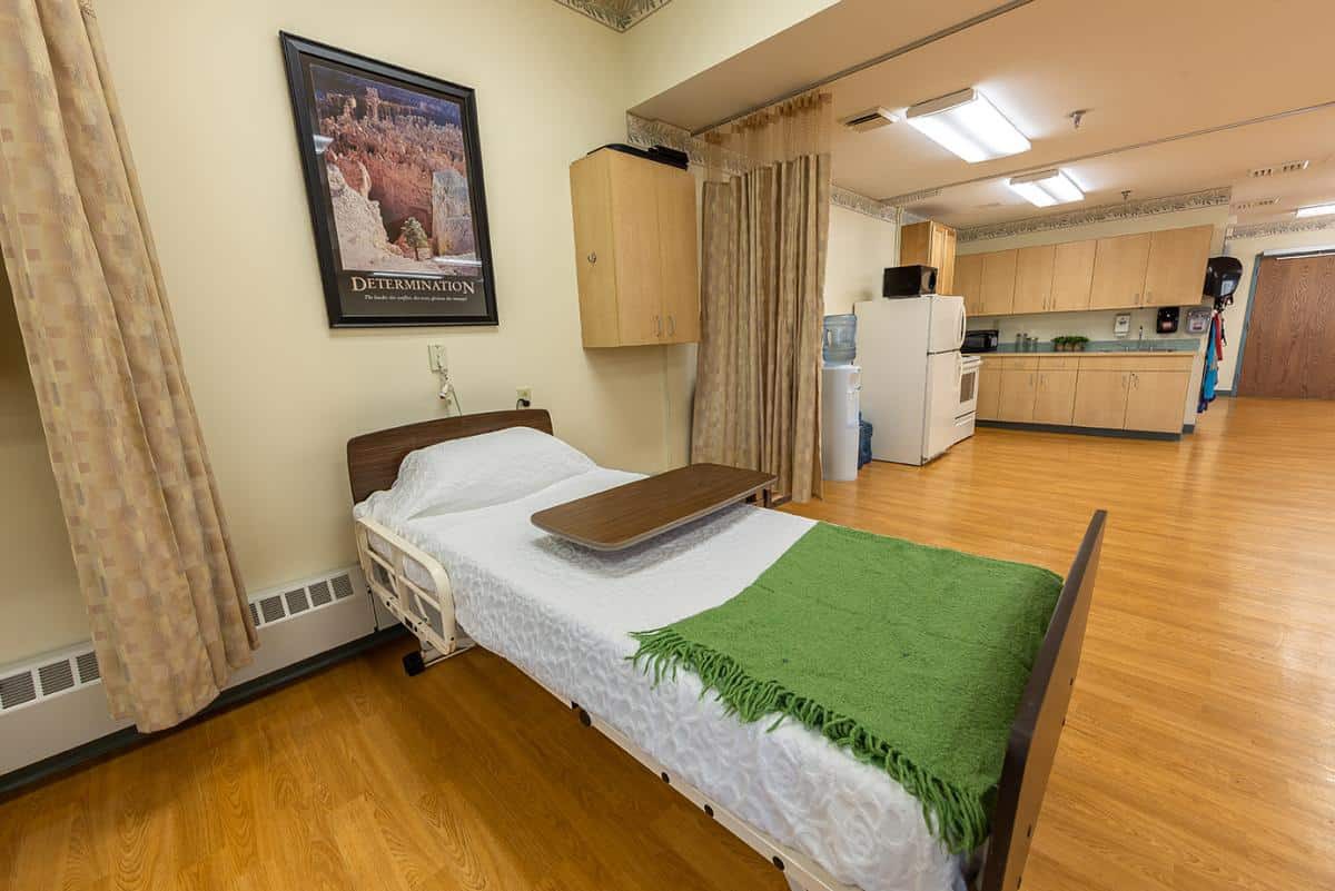 A clean and organized hospital room with a single bed and kitchenette.