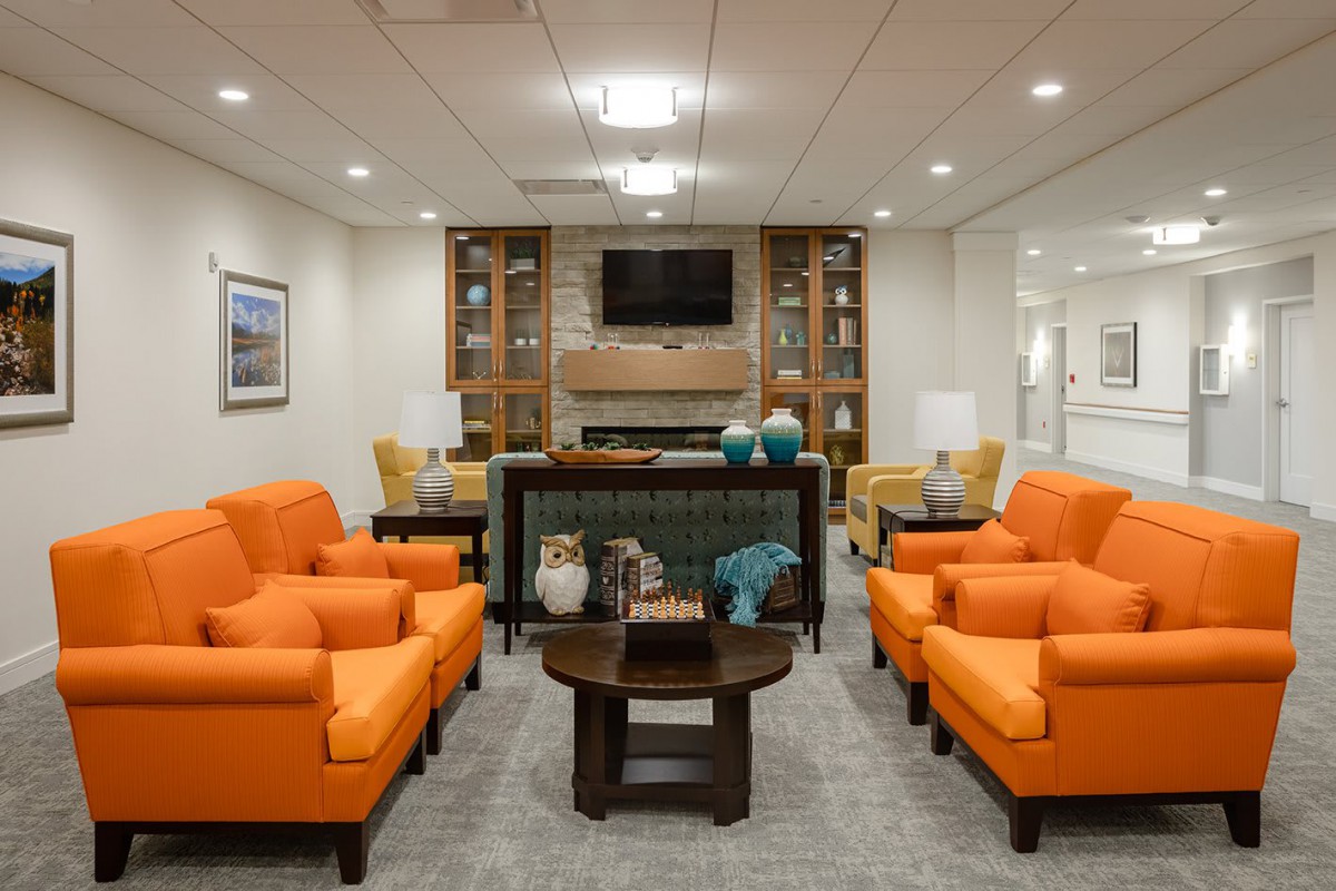 A modern living room featuring bright orange sofas and a sleek design with a television mounted over a fireplace.