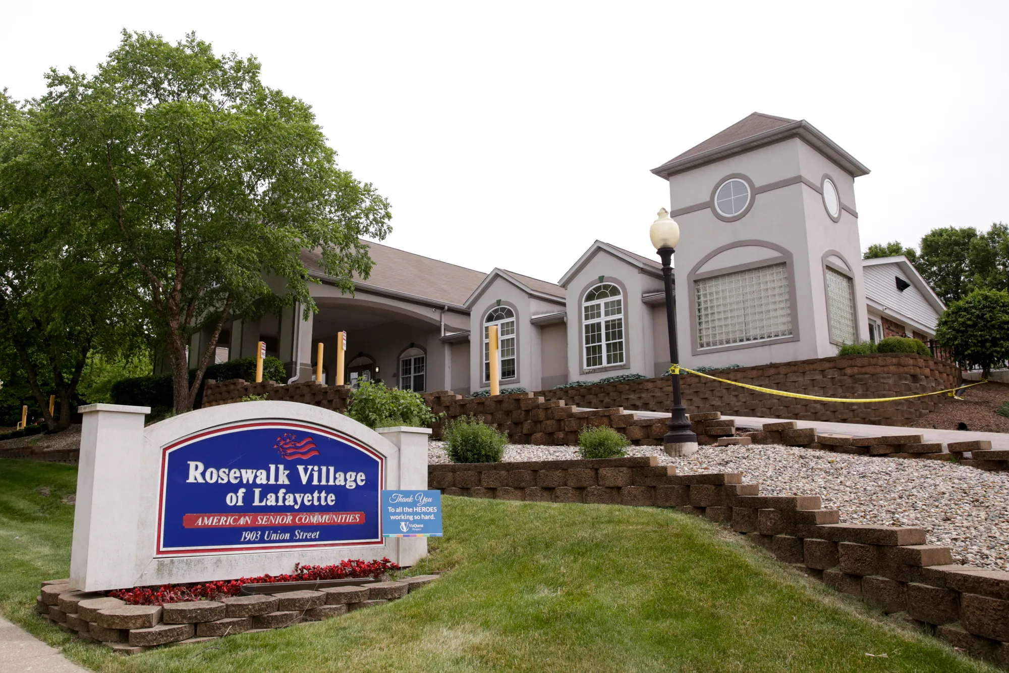 Exterior view of a senior living facility with a welcoming sign and landscaped surroundings.