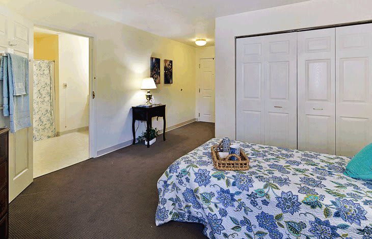 A cozy bedroom with a floral-patterned blanket, bedside table, and closet.