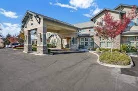 The image shows the entrance of a modern building with a covered driveway and landscaped surroundings.
