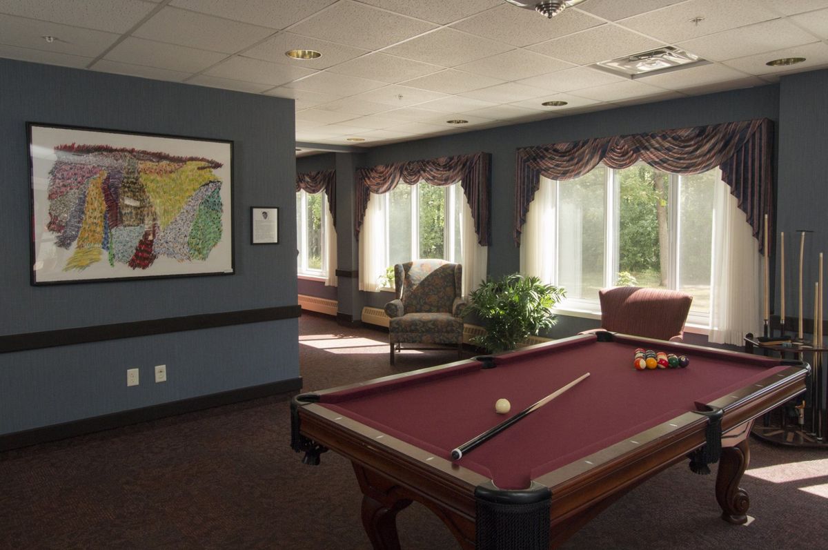 A cozy billiards room with a pool table and seating area bathed in natural daylight.